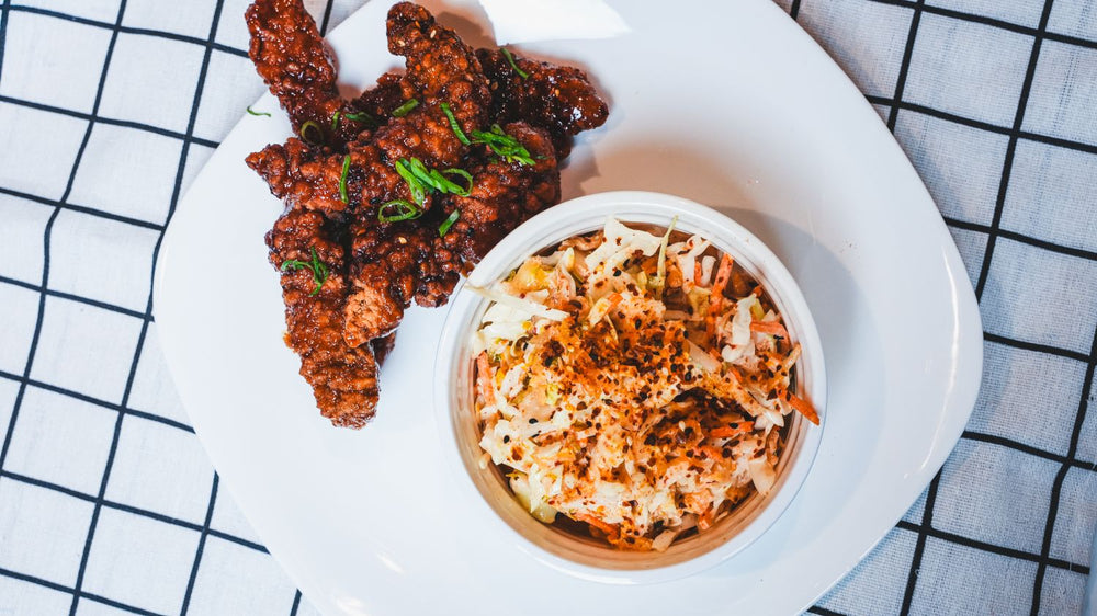 Glazed and charred chicken wings with a side on a white plate with a plaid cloth