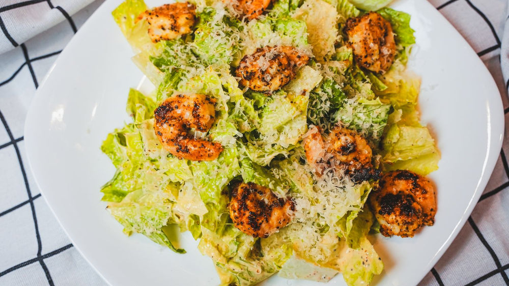 Overhead view of a Caesar salad with grilled shrimp and shaved cheese on a white plate