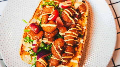 Loaded sausage topped with fresh vegetables and a sweet drizzle served on a white plate
