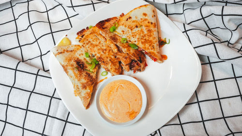 Overhead view of quesadilla wedges with a dipping sauce on a white plate with a plaid cloth