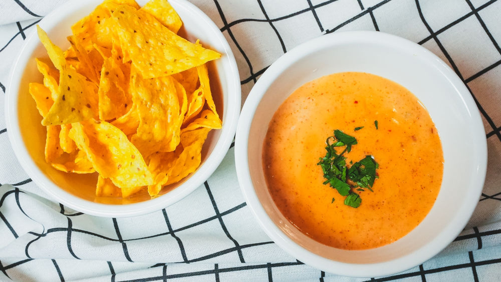 Overhead view of tortilla chips beside a bowl of tomato soup or queso dip on a white plate