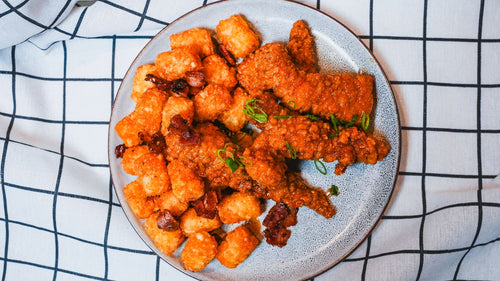 Overhead view of crispy fried chicken tenders and tater tots on a white plate with a plaid cloth