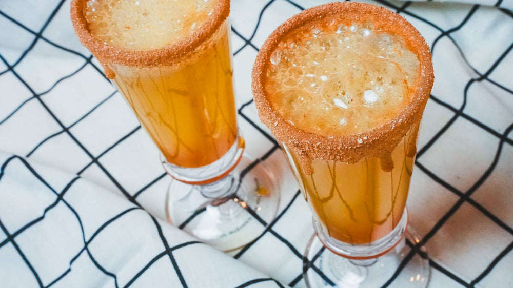 Two glasses of amber-colored frozen drinks on a plaid cloth background