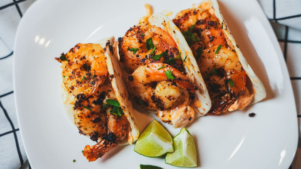 Overhead view of shrimp tacos arranged on a white plate next to lime wedges