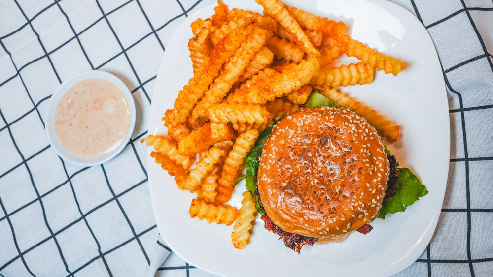 Overhead view of a burger with waffle fries and dipping sauce on a white plate