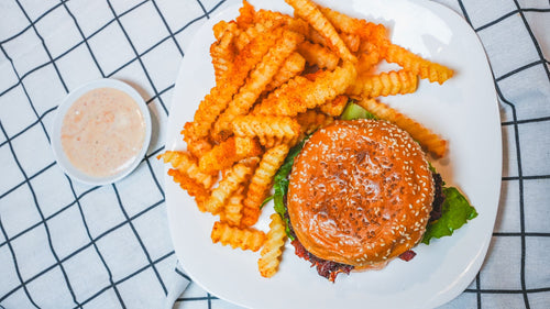 Overhead view of a burger with waffle fries and dipping sauce on a white plate