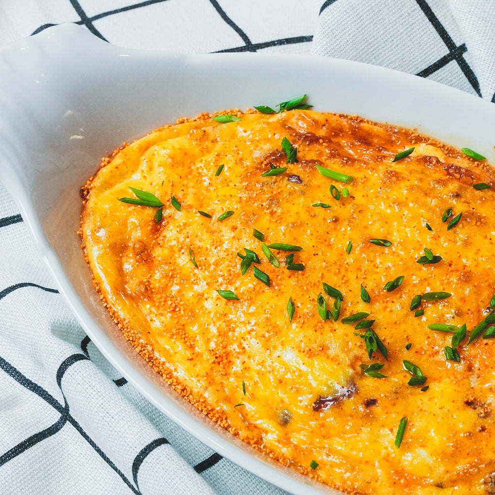 Overhead view of a cheesy egg frittata garnished with green onions on a white plate