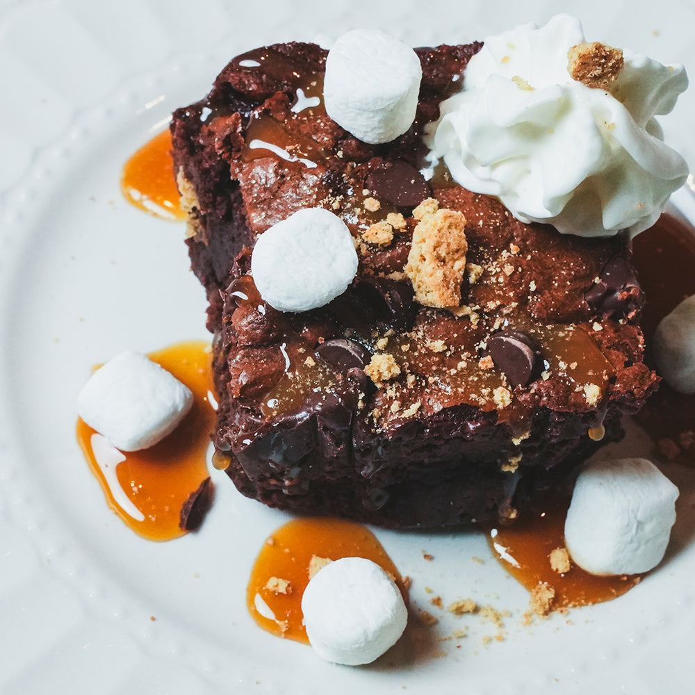Dark chocolate brownie with caramel drizzle and a scoop of cream on a white plate