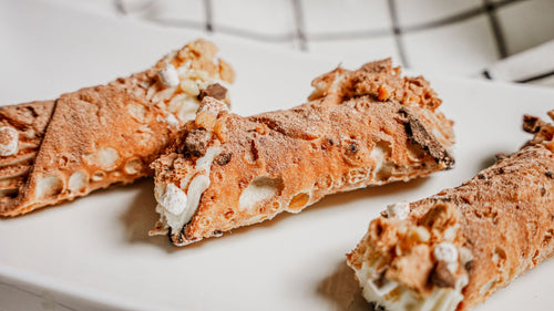 Three cannoli shells with cream on a white plate