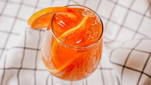 Glass of orange cocktail with an orange slice on a checkered tablecloth