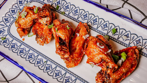 Baked chicken wings with a spicy sauce on a decorative platter.