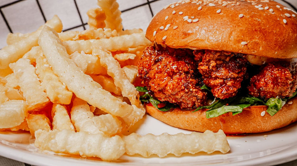Nashville Hot Chicken Sandwich featuring a Crispy fried chicken tossed in Spiceology's Nashville Hot Chicken seasoning, stacked on a soft bun with classic pickles, creamy slaw, and a swipe of mayo and fries on a white plate with a checkered tablecloth.