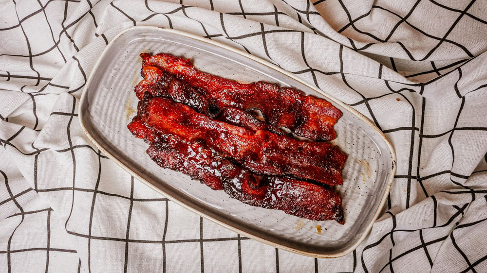 Candied Bacon featuring Thick-cut bacon sprinkled with Spiceology's Smoky Honey Habanero seasoning and roasted until caramelized on a tray with a checkered cloth background