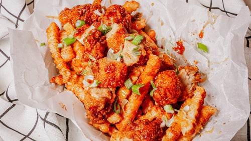 Baked cauliflower wings and fries with red sauce and green onions on a white paper-lined basket.