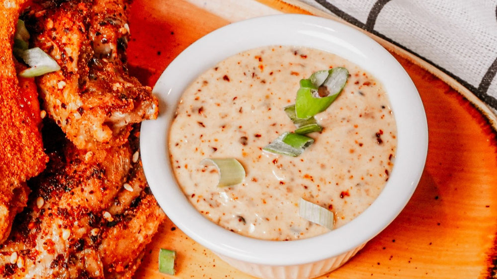 Bowl of creamy dipping sauce with green onions next to fried chicken on a wooden board.