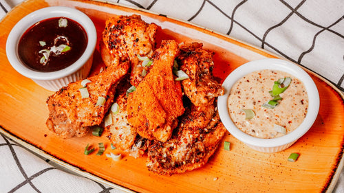 Platter of fried chicken with two dipping sauces on a wooden board.