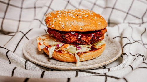 Hamburger with a sesame seed bun on a white plate over a checkered tablecloth