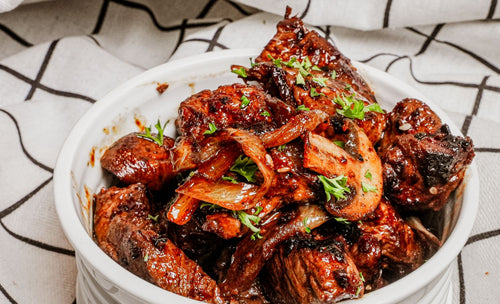 Stir-fried mushrooms and beef with a dark sauce in a white bowl on a patterned tablecloth.