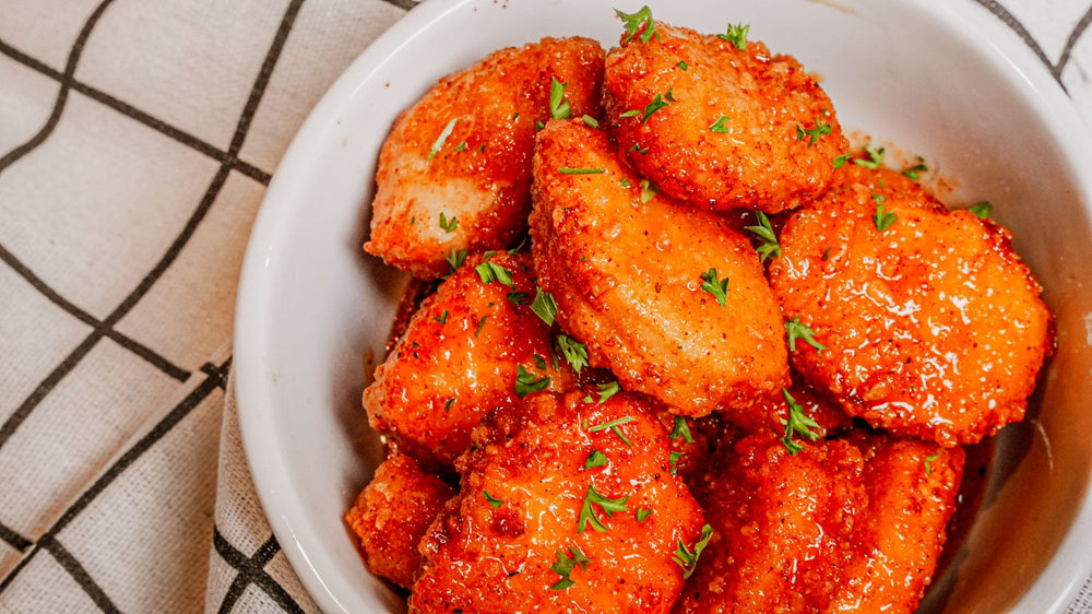 Smoky Honey Habanero Chicken Nuggets featuring Crispy fried chicken nuggets tossed in Spiceology's Smoky Honey Habanero seasoning for a glossy sweet-heat finish that balances smoky depth with chile warmth on a white plate with a checkered cloth background