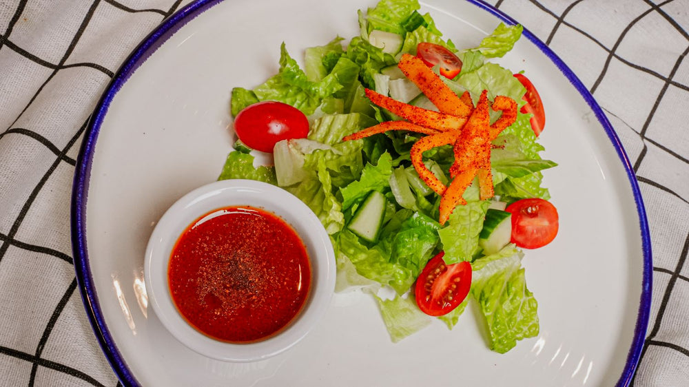 Mango Tango Citrus Vinaigrette featuring A bright citrus vinaigrette emulsified with Spiceology's Mango Tango chamoy-style seasoning for a vibrant balance of tropical sweetness, tangy acidity, and subtle chile heat on a white plate with a blue rim, served with a red dressing.