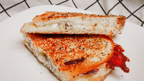 Grilled cheese sandwich cut in half on a white plate with a checkered tablecloth in the background