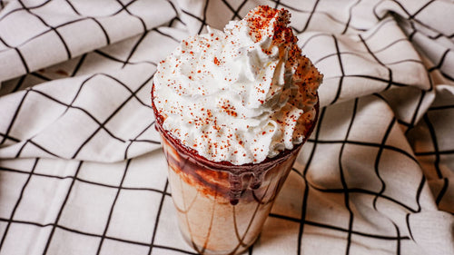 Chocolate drink with whipped cream and chili flakes on a checkered fabric background