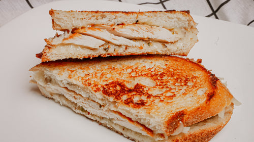 Grilled cheese sandwich cut in half on a white plate with a checkered cloth background