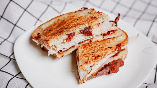 Grilled cheese sandwich cut in half on a white plate with a checkered cloth background