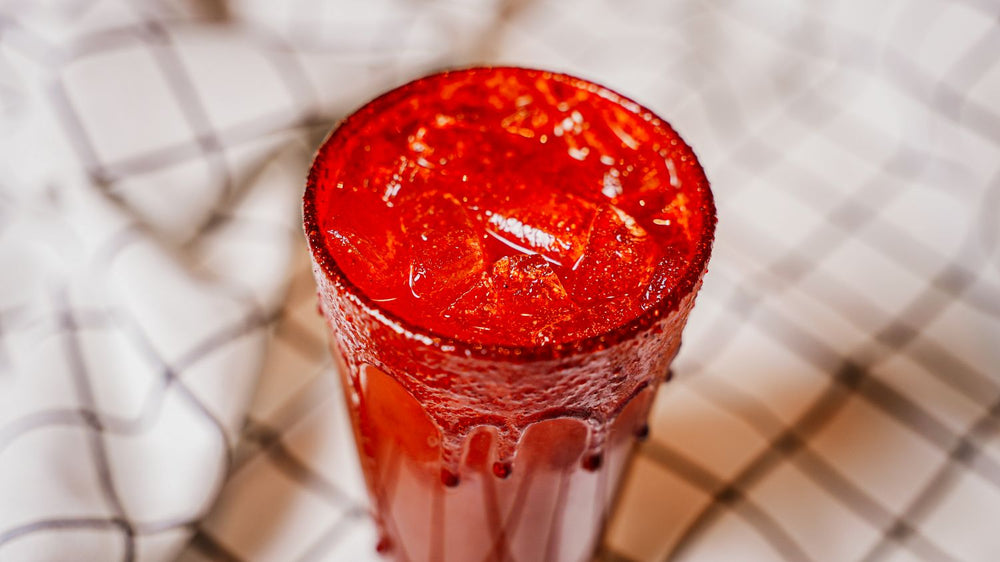 Mango Chile Lemonade featuring Lemonade layered with a chamoy-style paste — Spiceology's Mango Tango seasoning plus water — then stirred for balanced sweet heat in every sip. Finished with a bold Mango Tango rim in a glass with a checkered background