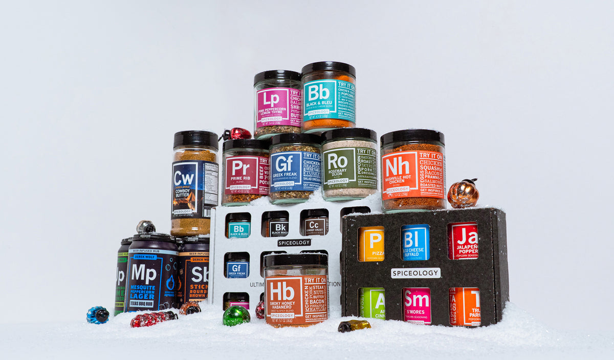 Spiceology jars, the Ultimate Rub Collection, a popcorn seasoning six-pack and Derek Wolf rub cans stacked in snow with glass ornaments