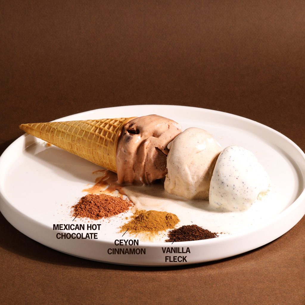 3 scoops of ice cream on a white plate with brown background and piles of spices next to it