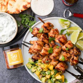 chicken on skewers with lime, avocado mango relish, tzatziki, naan bread, beer and a jar of spices