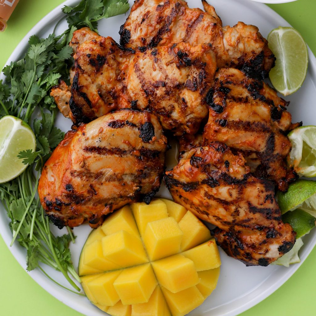a plate of grilled mango chicken on a white plate with a green background