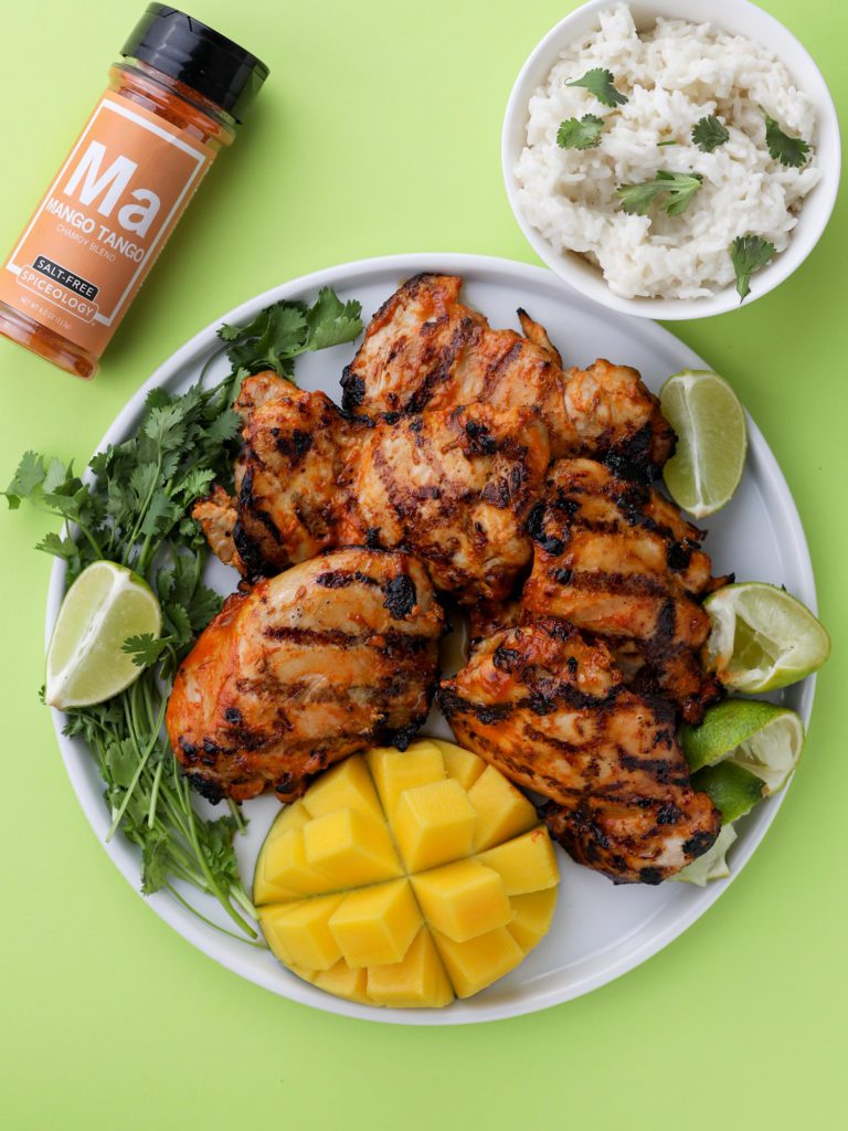 a plate of grilled mango chicken on a white plate with green background