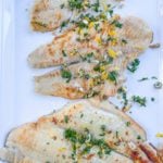 a white platter with petrale sole fillets and a parsley gremolata on top