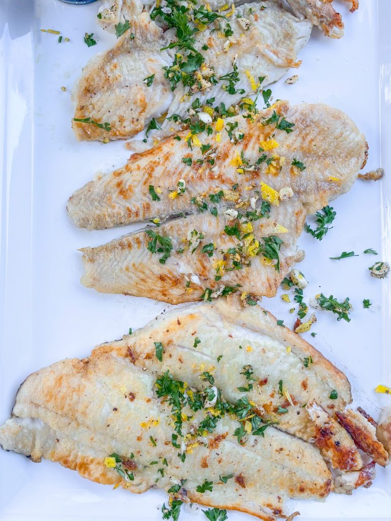 a white platter with petrale sole fillets and a parsley gremolata on top
