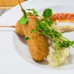 Bratwurst corn dogs on plate with tomato jam, sauerkraut and sprouts