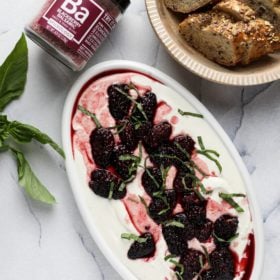 a plate of whipped feta dip with roasted blackberries, bread and a jar of spice