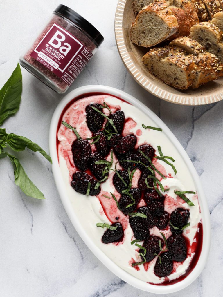 a plate of whipped feta topped with roasted blackberries with bread and a jar of spice