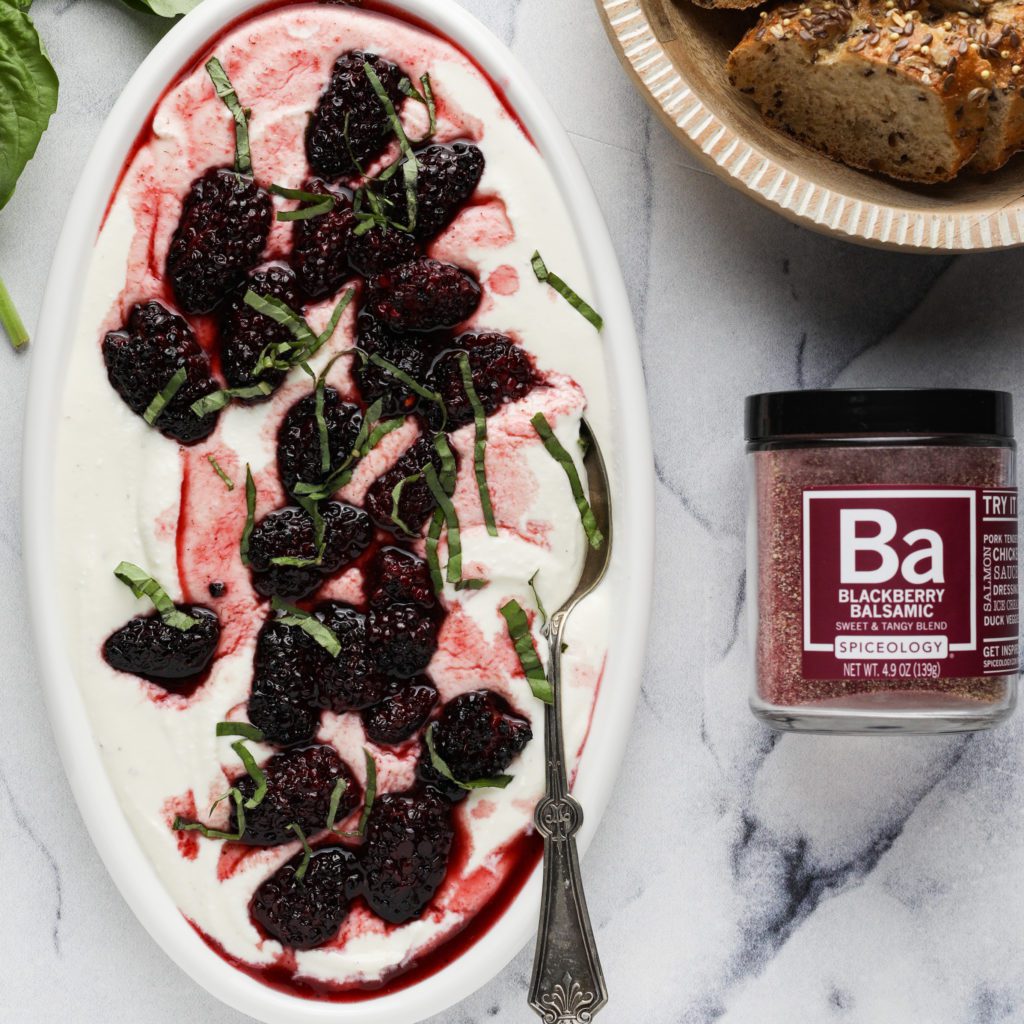 a plate of whipped feta with roasted blackberries, bread and a jar of spice