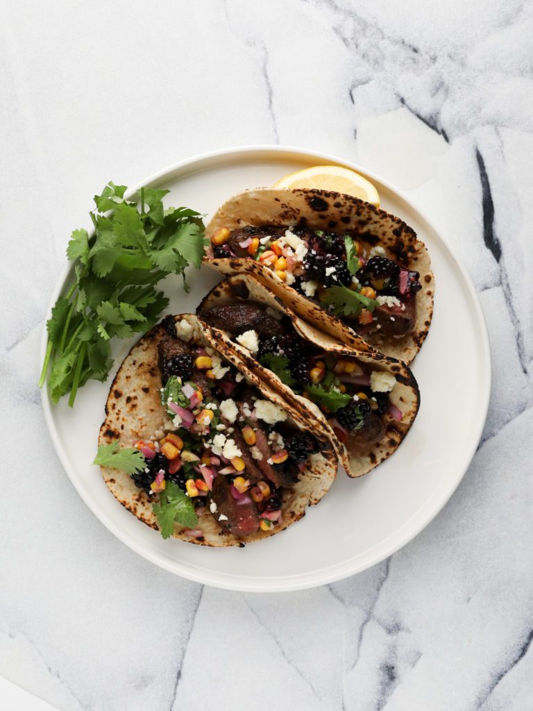 flat iron steak tacos with blackberry salsa on a white background