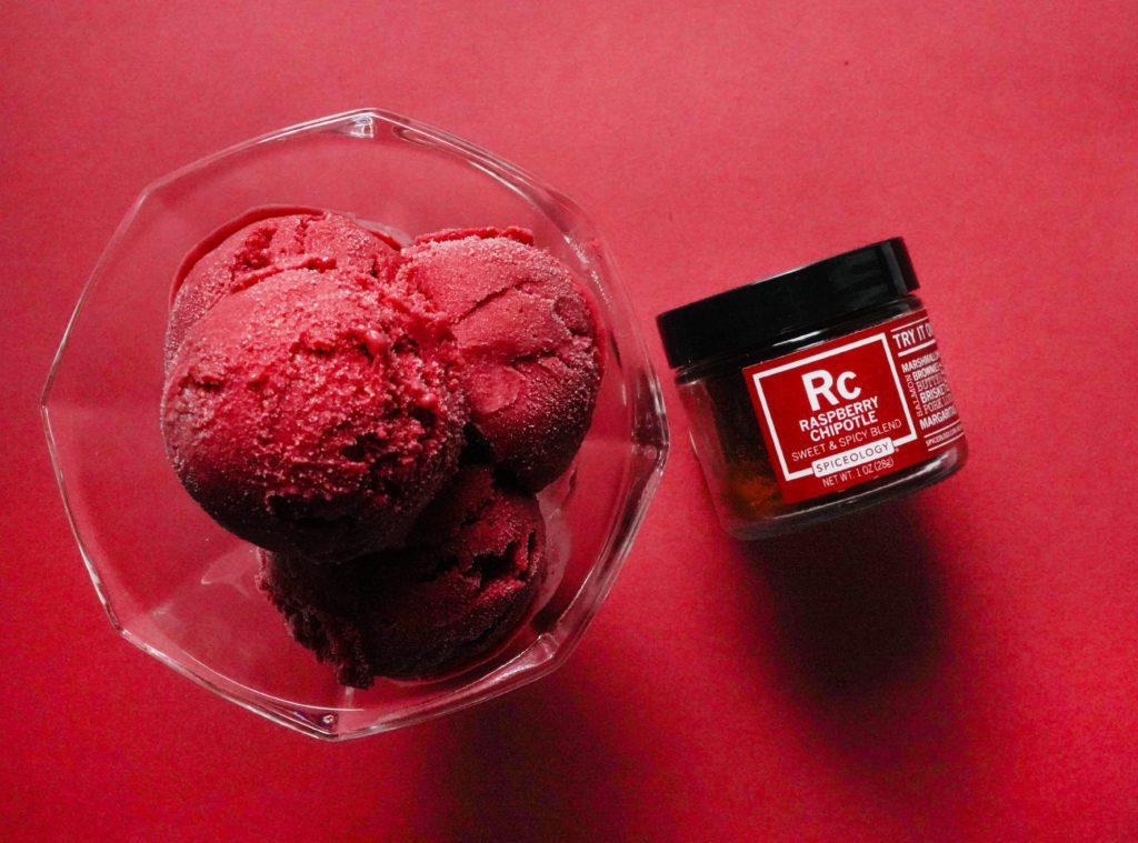 raspberry chipotle sorbet in bowl on red background with jar of raspberry chipotle