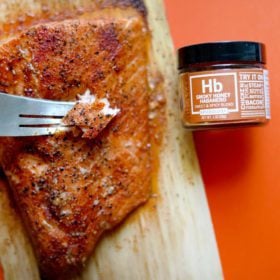 smoky honey habanero cedar plank salmon served on plank with fork bite and jar of spices